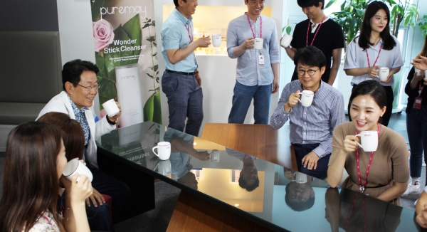 (*직원들과 머그컵으로 커피를 마시고 있는 임직원들과 김국현 대표