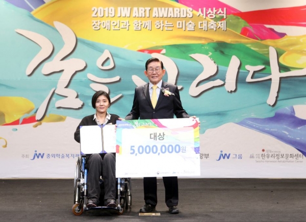 JW그룹 이종호 명예회장(오른쪽)이 대상 수상자 최지현 씨에게 ‘2019 JW 아트 어워즈’ 대상을 수여하고 기념촬영을 하고 있다.